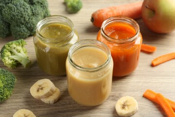 Tasty baby food in jars and ingredients on wooden table