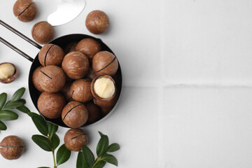 Tasty Macadamia nuts and green twigs on white tiled table, flat lay. Space for text