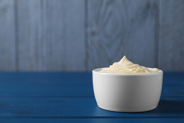 Tasty mayonnaise in bowl on blue wooden table, space for text