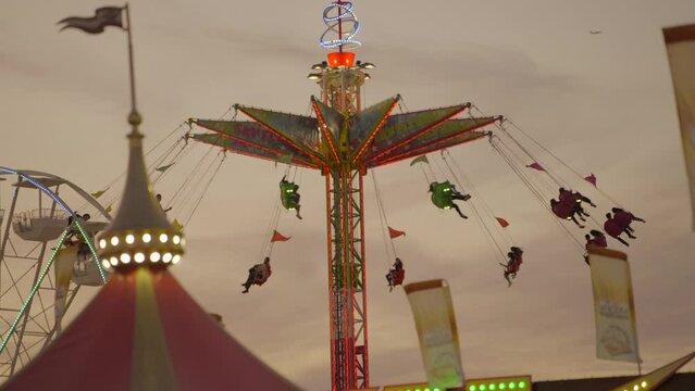 This video shows an epic spinning chair ride with an evening sky in the background at a carnival fair. 