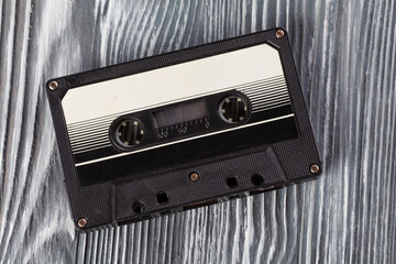 Black audio cassette on the gray wooden background. Vintage, retro style. Soft focus.