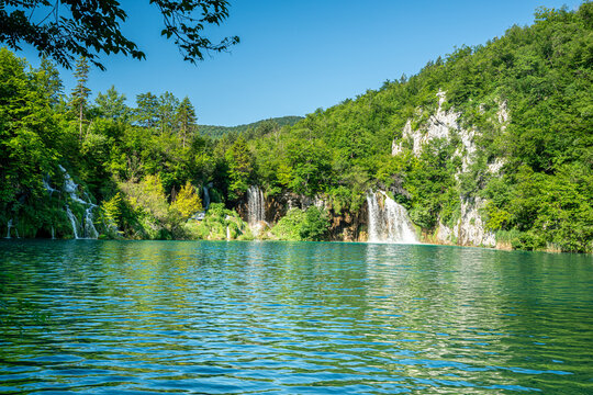 Wasserf&auml;lle Nationalpark Plitvicer Seen, Kroatien. See im Vordergrund, H&uuml;gel mit B&auml;umen und B&uuml;schen im Hintergrund am Tag.