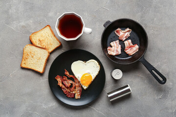 Composition with tasty bacon, fried egg, toasts and cup of tea on grey background