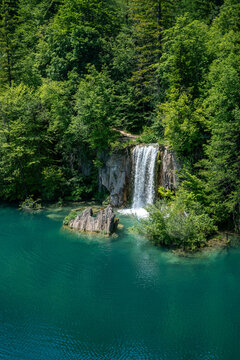 Nationalpark Plitvicer Seen, Kroatien. Wasserfall umrahmt von B&auml;umen im Vordergrund ein See mit Felsen am Tag