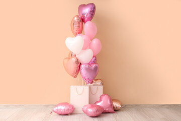 Heart-shaped balloons with shopping bags near beige wall. Valentine's Day celebration