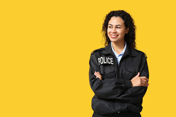 Beautiful young happy African-American policewoman on yellow background