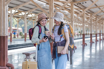 Fototapeta na wymiar Two Asian female tourist friends are at the train station. Waiting for the train to travel to the provinces together on the weekend.