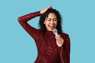 Beautiful young happy African-American female singer with microphone singing on blue background - obrazy, fototapety, plakaty