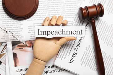 Wooden hand with word IMPEACHMENT and judge gavel on newspapers, closeup