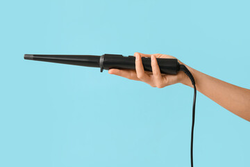 Hand of young woman with curling iron on blue background