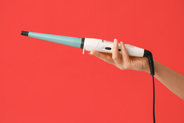 Hand of young woman with curling iron on red background