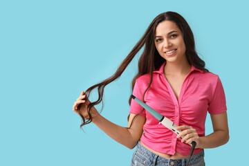 Beautiful young woman with curling iron on blue background