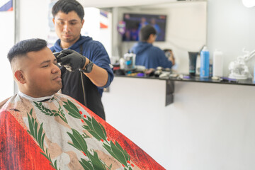 Smiling client sitting while latin barber cutting his hair