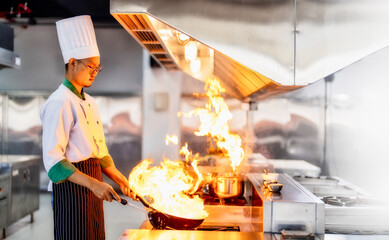Chef in restaurant kitchen at stove and pan cooking flambe on food.