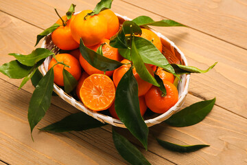 Wicker bowl with sweet mandarins and leaves on wooden background