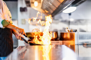 Chef in restaurant kitchen at stove and pan cooking flambe on food