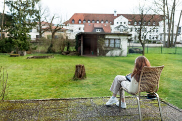 A young woman in headphones with a digital tablet looks at the screen of a gadget, video, film, call. A teenager sits on a chair in the backyard of a house on a sunny warm day. High quality 4K footage