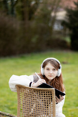 A young woman in headphones with a digital tablet looks at the screen of a gadget, video, film, call. A teenager sits on a chair in the backyard of a house on a sunny warm day. High quality 4K footage