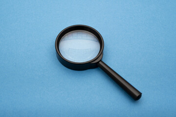 a magnifying glass on blue paper, essence of a searching engine concept quest for information and...