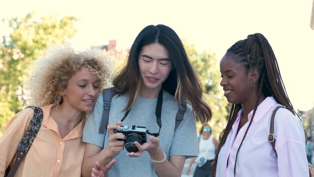 Three multiracial friends looking at the photos in a camera while sightseeing in Madrid, Spain.