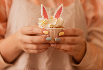 Close-up of female hands with a neat manicure hold a baby cake. Delicious cute cupcake with rabbit...