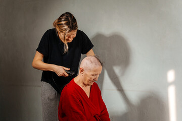 shaving woman because of a cancerous tumor. removal of hair on the head with an electric razor before surgery. hair loss due to cancer. shaving the grandmother's head before a course of chemo therapy - obrazy, fototapety, plakaty