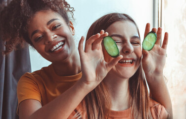 Close up above photo of two best girlfriends spending time together having fun while applying cucumber slices on eyes holding them with hands