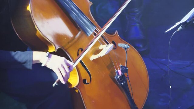 Close-up of cello playing. A woman's hand with a bow playing classical music on a cello. Bright light show. Slow motion
