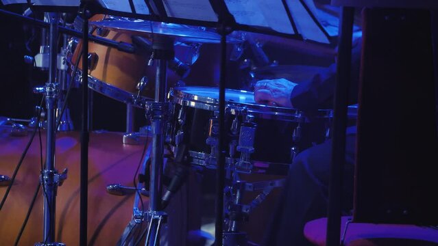 Drummer playing drums at a concert. The musician beats a stick on the edge of the working drum. Slow composition. A light show. Close-up