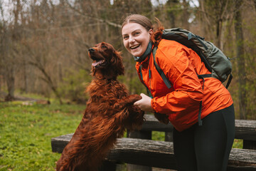 Young happy woman with sport backpack resting traveling with dog. A young female hugs her beloved...