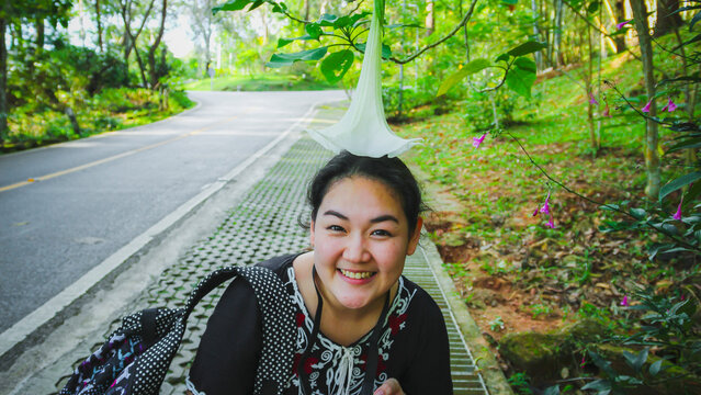 Asian female tourist takes photo with flowers on the side of the road at the edge of the forest.
