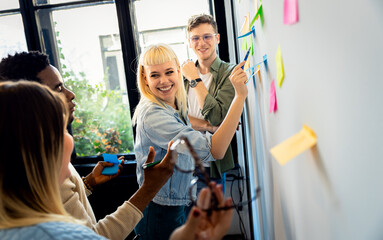 Diverse group of young business people working in office using colorful sticky notes on wall to...