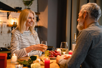 Adorable middle-aged couple looking each other into their eyes during romantic dinner in the kitchen on St. Valentines Day