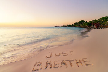 Handwritten Just breathe on sandy beach at sunset - obrazy, fototapety, plakaty
