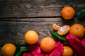 Mandarines with leaves and red wrapping paper on rustic aged wooden background.