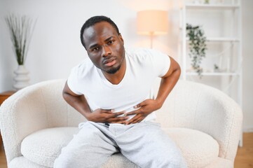 Black Man Having Stomachache Suffering From Painful Abdominal Spasm Standing Touching Aching Abdomen At Home