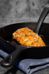Pan fried breaded haddock fish in a cast iron frying pan. On a dark stone background