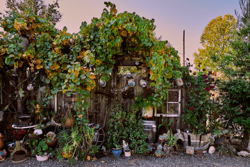 A fence overgrown with greenery and adorned with antiques and garden art