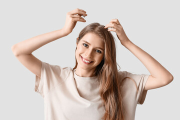 Young woman using serum for hair growth on light background