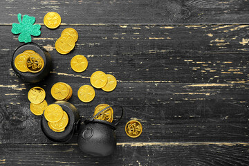 Pots with golden coins and paper clover on black wooden background. St. Patrick's Day celebration