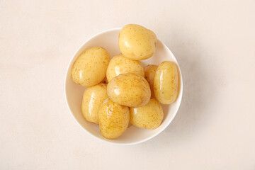 Bowl with raw potatoes on light background