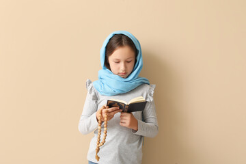 Little Muslim girl with Quran and praying beads on beige background