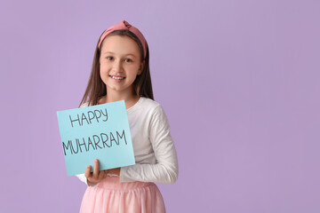 Little Muslim girl with greeting card for Islamic New Year on lilac background