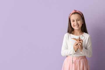 Little Muslim girl with Aladdin lamp on lilac background