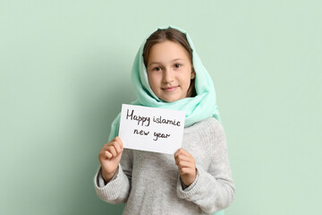 Little Muslim girl with greeting card for Islamic New Year on light background