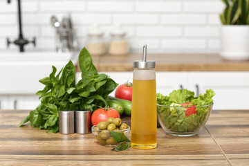 Bottle with oil, olives, vegetables and fresh salad on table in kitchen