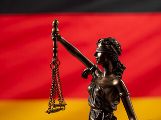 Bronze statue of justice with the German flag in the background. German law concept.