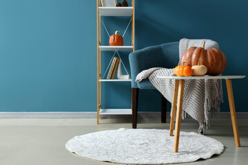 Interior of stylish living room with armchair, pumpkins on coffee table and shelving unit