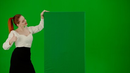 Portrait of attractive office girl on chroma key green screen. Woman in skirt and blouse pointing at green advertisement board, shows thumbs up.