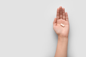 Naklejka premium Female hand with white capsule on light background